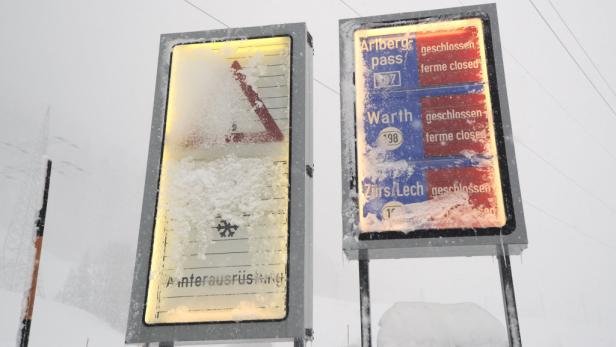Zwei Schilder, die teilweise mit Schnee bedeckt sind, zeigen Informationen zu gesperrten Bergpässen.