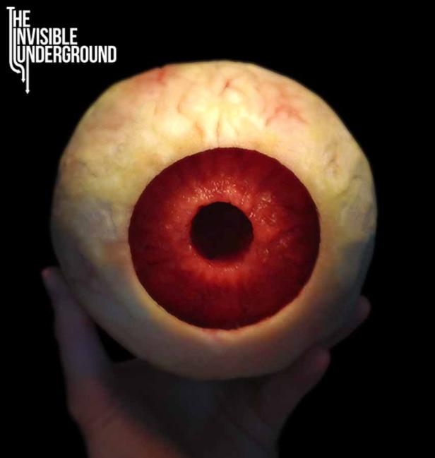 Eine Hand hält einen großen, künstlichen Augapfel mit roter Iris.