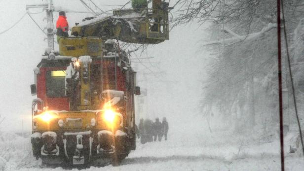 Ein gelb-rotes Schienenfahrzeug mit Arbeitsbühne steht im Schneefall.