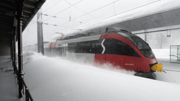 Ein roter Zug der ÖBB steht im Schnee an einem Bahnsteig.