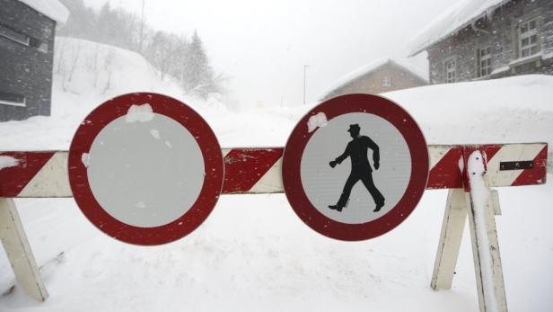 Eine Straßensperre mit Verkehrszeichen steht im Schnee.