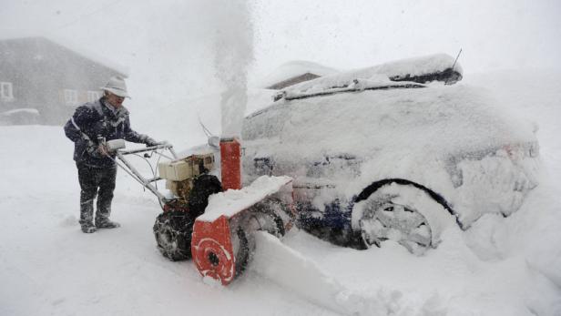 Eine Person räumt mit einer Schneefräse Schnee von einem Auto.