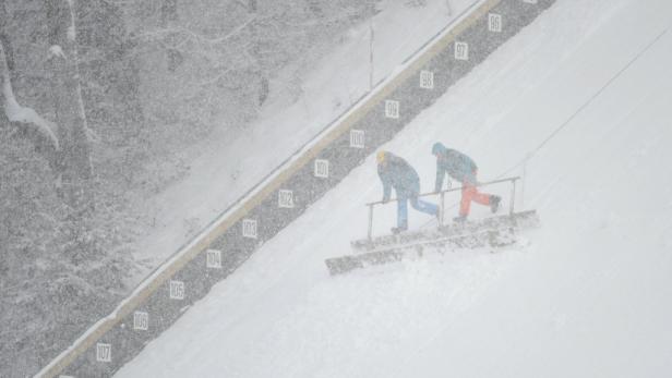 Zwei Personen stehen während eines Schneesturms auf einem Skisprungturm.
