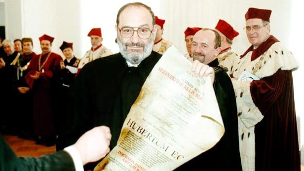 Ein Mann mit Brille hält eine Urkunde bei einer akademischen Zeremonie.