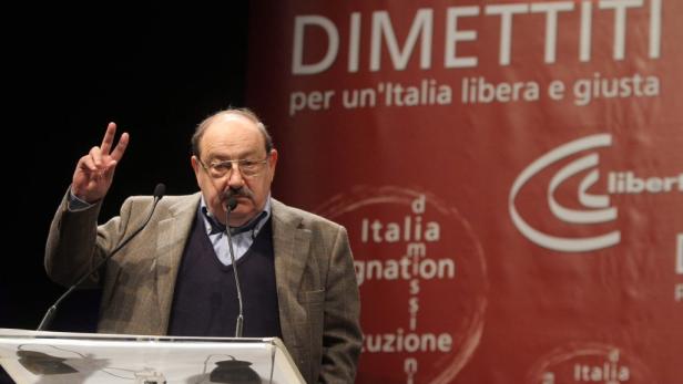 Ein Mann mit Brille und Schnurrbart hält eine Rede und zeigt das Friedenszeichen.