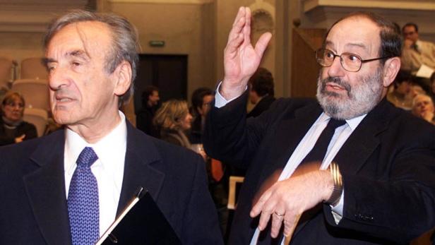 Zwei Männer in Anzügen stehen vor einer Menschenmenge, einer hebt die Hand.