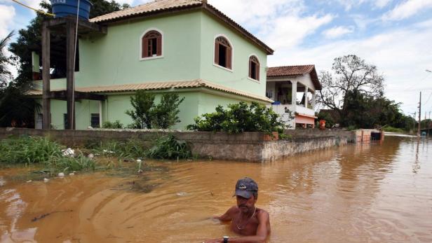 Ein Mann watet durch das hochwasserartige Wasser vor einem hellgrünen Haus.