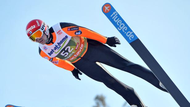 Ein Skispringer in der Luft vor blauem Himmel.