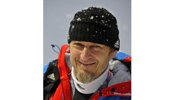 Ein lächelnder Mann mit Bart und Mütze, bedeckt mit Schneeflocken.