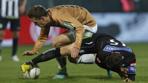 Zwei Fußballspieler kämpfen um den Ball auf dem Spielfeld.
