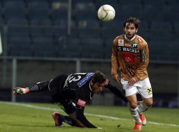 Zwei Fußballspieler während eines Spiels, einer rutscht auf dem Rasen, der andere steht daneben.