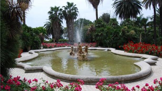 Ein Brunnen mit einer Figurengruppe in einem üppigen Garten.