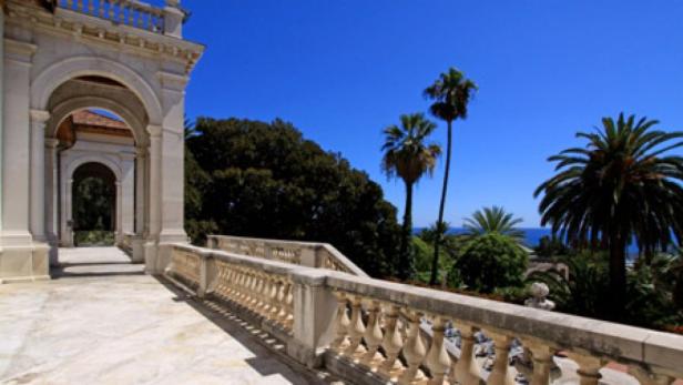 Ein Blick von einer Terrasse mit Balustrade auf Palmen und das Meer.