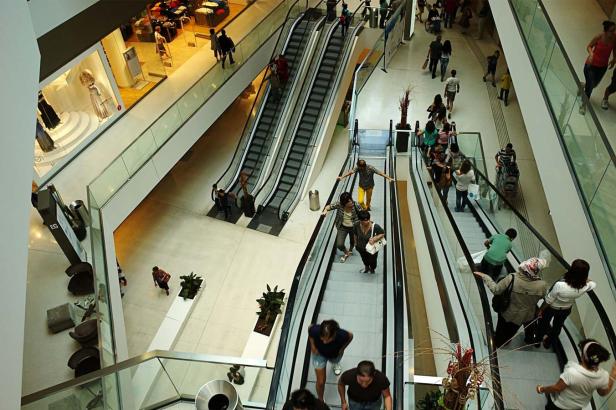 Mehrere Personen fahren in einem Einkaufszentrum auf Rolltreppen.