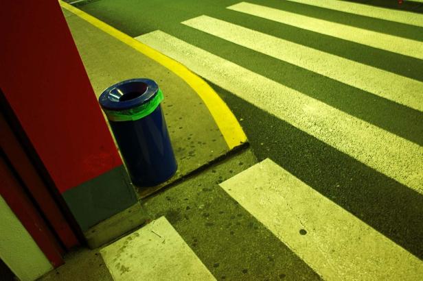 Ein blauer Mülleimer steht neben einem Zebrastreifen.