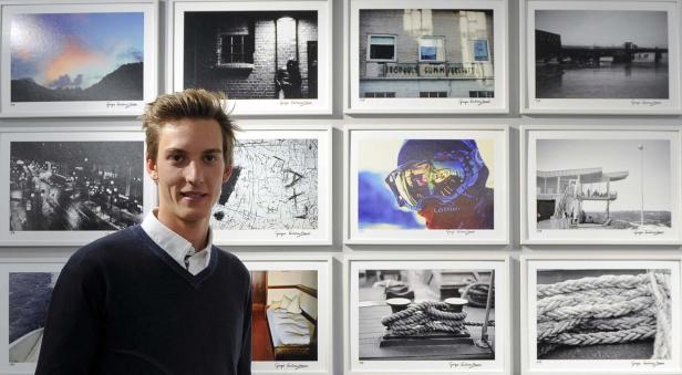 Ein junger Mann steht vor einer Wand mit gerahmten Fotografien.