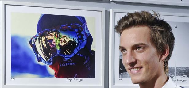 Ein junger Mann steht neben einem gerahmten Foto eines Skifahrers mit reflektierenden Skibrillen.