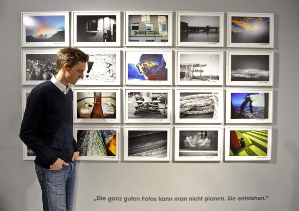 Ein Mann betrachtet eine Wand mit gerahmten Fotografien in einer Galerie.