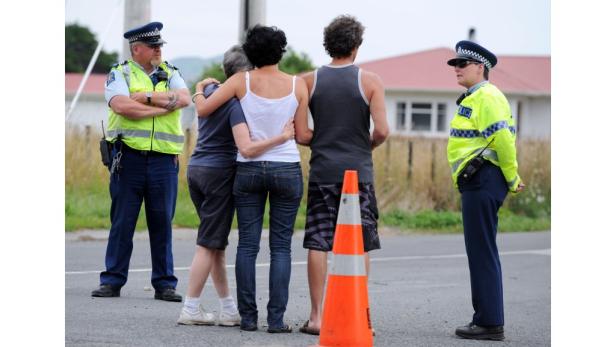 Zwei Polizisten stehen neben einer Gruppe von drei Personen, die sich umarmen, an einer Straße.