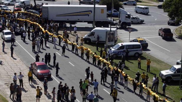 Menschen bilden eine lange Kette mit einem gelben Band auf einer Straße.