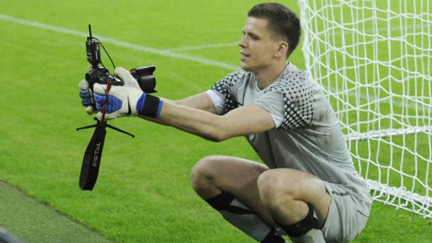 Ein Fußballtorwart hockt auf dem Rasen und fotografiert mit einer Digitalkamera.