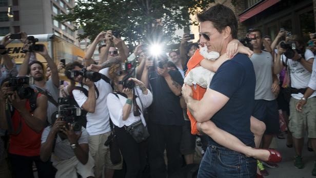 Tom Cruise trägt ein Kind auf dem Arm, umringt von Fotografen.