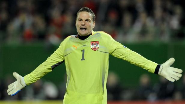 Ein österreichischer Fußballtorwart mit grünem Trikot und der Nummer 1 steht mit ausgestreckten Armen auf dem Feld.