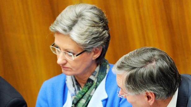 Eine Frau mit Brille und blauem Blazer sitzt neben einem Mann im Anzug.