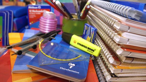 Ein Stapel Notizbücher, ein gelber Textmarker und andere Schreibwaren liegen auf einem Tisch.