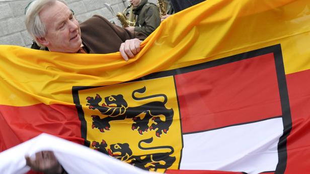 Ein Mann hält eine Flagge von Sachsen-Anhalt hoch, während im Hintergrund Saxophonspieler zu sehen sind.