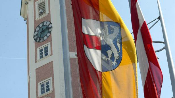 Eine Flagge mit einem Wolfswappen weht vor einem Turm mit einer Uhr.