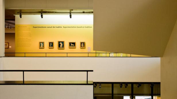 Innenansicht eines Museums mit Gemälden an einer gelben Wand.