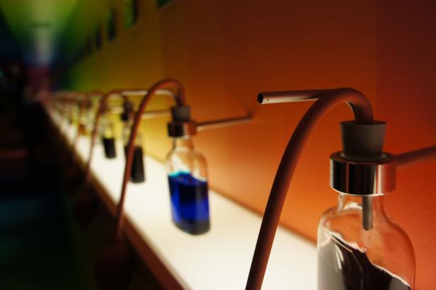 Eine Reihe von Glasflaschen mit farbigen Flüssigkeiten und angeschlossenen Schläuchen stehen auf einem Regal.