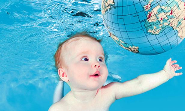 Ein Baby schwimmt unter Wasser und greift nach einem Globus.