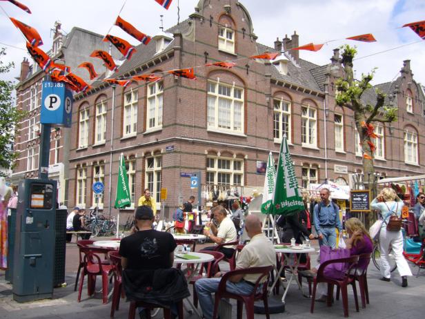 Ein belebter Marktplatz in den Niederlanden mit orangefarbenen Flaggen und Menschen an Tischen.