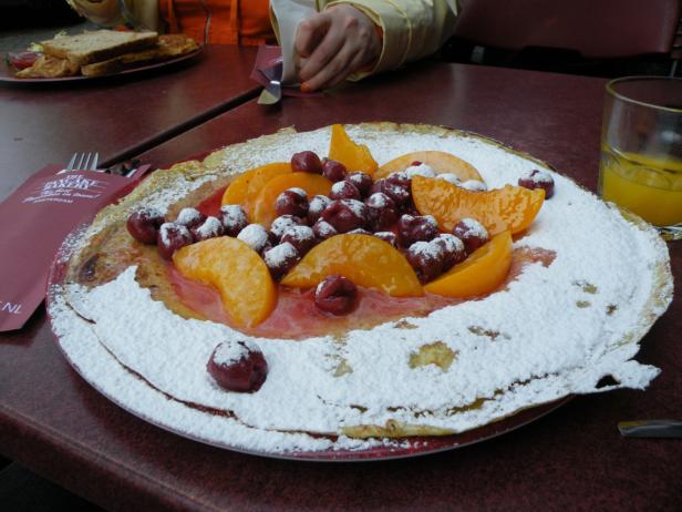 Ein mit Puderzucker, Pfirsichspalten und Kirschen belegter Pfannkuchen wird serviert.