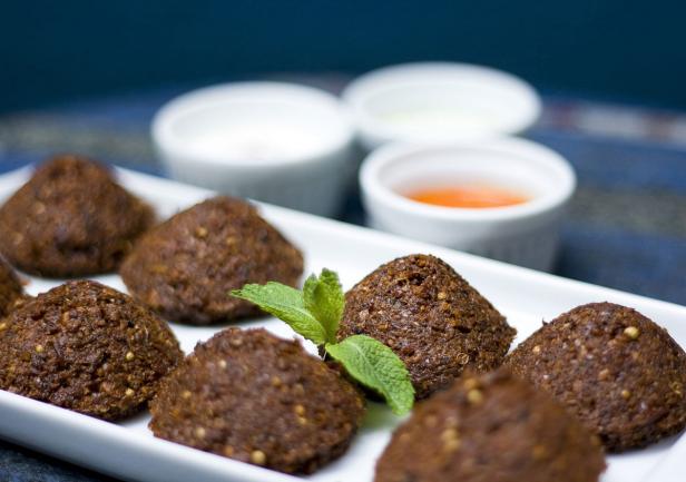 Eine Platte mit Falafel und Dipsaucen, garniert mit einem Minzzweig.