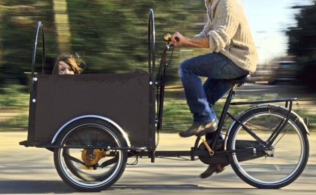 Ein Mann fährt ein Lastenfahrrad, in dem ein Mädchen sitzt.