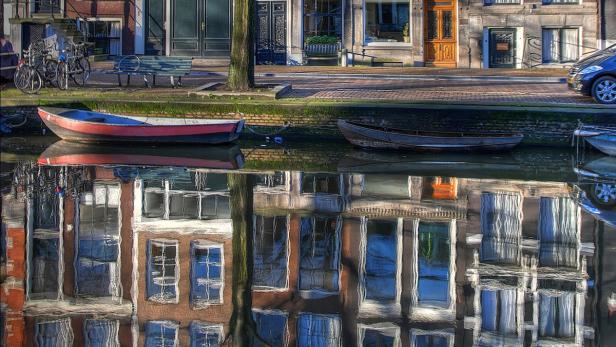 Boote liegen an einem Kanal in Amsterdam, die sich im Wasser spiegeln.