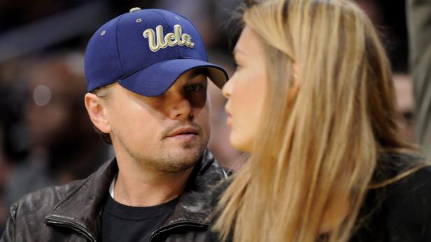 Leonardo DiCaprio mit einer Frau im Gespräch, er trägt eine UCLA-Kappe.