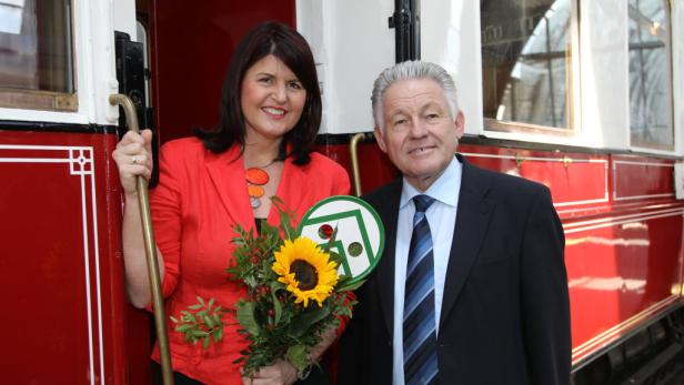 Eine Frau mit Sonnenblumenstrauß und ein Mann stehen vor einem roten Zug.