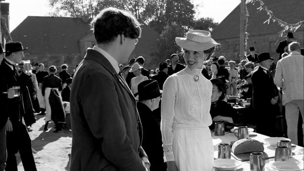 Eine Frau mit Hut und ein Mann unterhalten sich auf einer Veranstaltung im Freien.