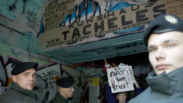 Polizisten stehen vor dem Kunsthaus Tacheles, während eine Person ein Schild mit der Aufschrift „Art we trust“ hochhält.