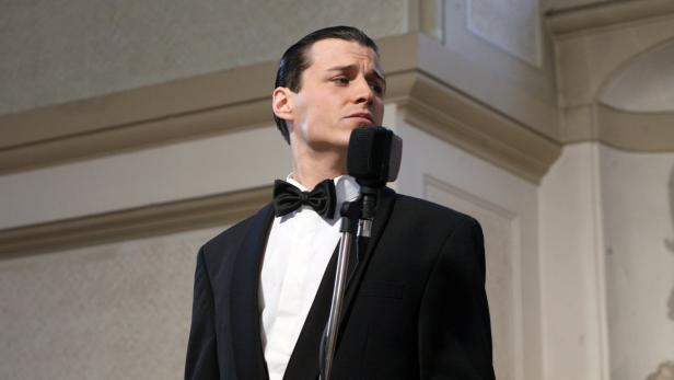 Ein Mann im Anzug mit Fliege singt in ein Mikrofon.