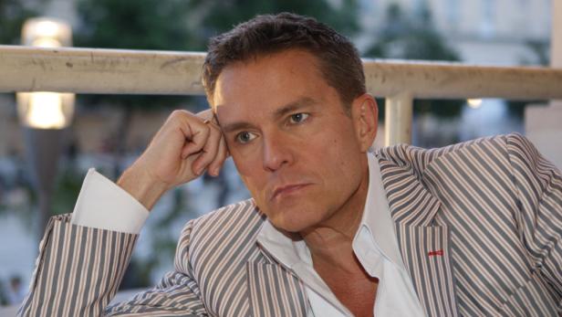 Ein Mann in einem gestreiften Sakko lehnt nachdenklich auf seinem Arm.