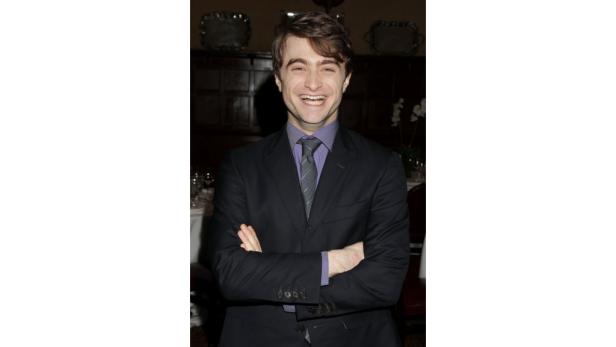 Daniel Radcliffe lächelt mit verschränkten Armen in einem dunklen Anzug.