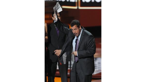 Adam Sandler hält eine Rede mit einem Blatt Papier in der Hand.