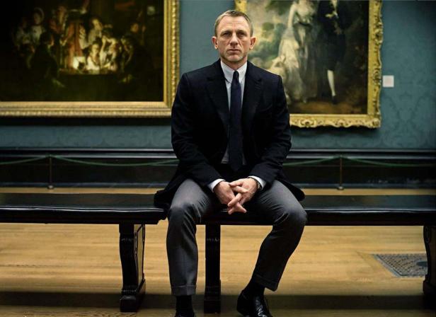 Daniel Craig sitzt in einer Kunstgalerie vor zwei Gemälden.