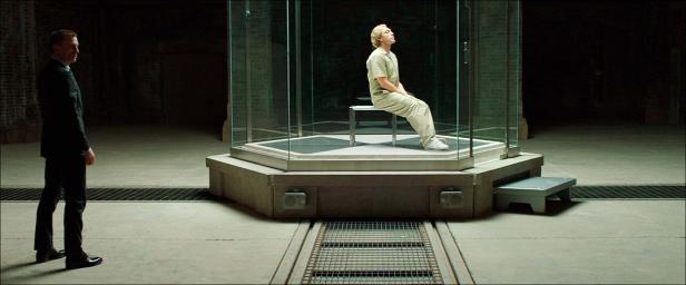 Ein Mann im Anzug beobachtet einen Mann in einem Glaskasten.