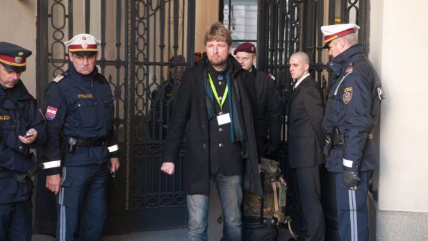 Ein Mann in Begleitung von mehreren Polizisten vor einem Gebäude.